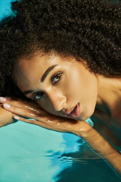 Retrato de mulher americana africana bonita com cabelo encaracolado olhando para a câmera e nadando na água — Fotografia de Stock