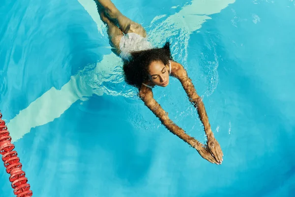 Top view of young african american woman swimming in clear and blue pool water, serene and peaceful — Stock Photo