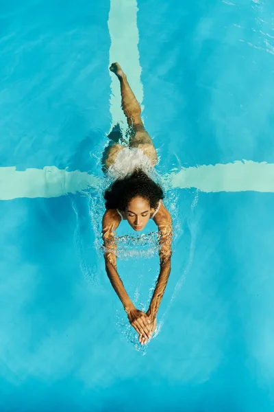 Blick von oben auf junge schwarze Frau, die in klarem und blauem Poolwasser schwimmt, ruhig und friedlich — Stockfoto