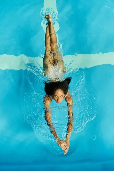 Vista superior de la joven afroamericana nadando en agua clara de la piscina, serena y tranquila - foto de stock