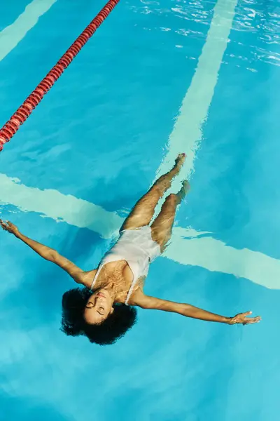 Top view of young and curly african american woman swimming on back in clear pool water, serenity — Stock Photo