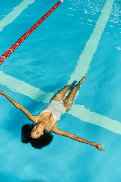 Top view of young african american woman swimming on her back in blue pool water, tranquility — Stock Photo