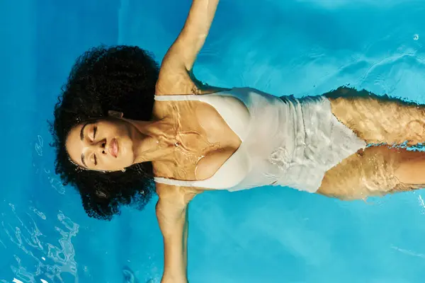Vista superior da mulher americana africana encaracolada nadando de costas em água clara da piscina, tranquilidade — Fotografia de Stock
