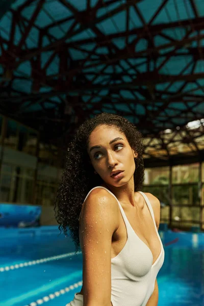 Jeune femme afro-américaine détendue avec les cheveux bouclés humides et la peau debout près de la piscine, sérénité — Photo de stock