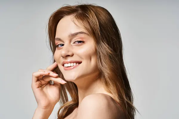 Fröhlich lächelnde Frau mit trendigem Make-up, Blick in die Kamera, Hände nah am Gesicht auf grauem Hintergrund — Stockfoto