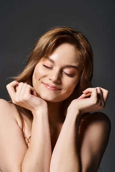Retrato de belleza de una atractiva joven sonriente con los ojos cerrados, posando sobre un fondo gris oscuro - foto de stock
