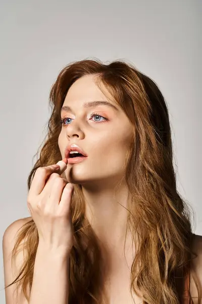 Schönheitsporträt einer hübschen Frau mit nacktem Make-up, die pfirsichfarbenen Lippenstift auf grauem Hintergrund aufträgt — Stockfoto