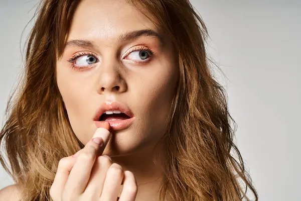 Closeup beauty shot of woman looking away with nude makeup applying lipstick on grey background — Stock Photo