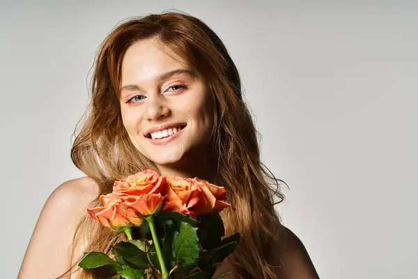 Retrato de una joven sonriente con ojos azules, sosteniendo rosas melocotonas posando sobre fondo gris - foto de stock