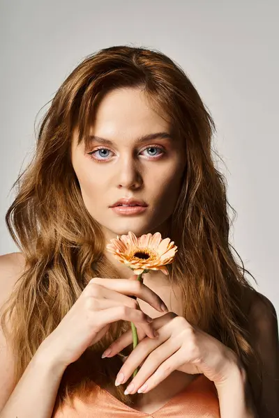 Foto de belleza de una mujer bonita con ojos azules, con gerberas cerca de la cara sobre fondo gris - foto de stock
