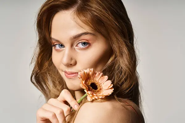 Side view of smiling attractive blue eyed girl, with gerbera daisy near face on grey background — Stock Photo