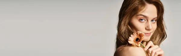 Vue latérale d'une jolie fille souriante, avec marguerite gerbera près du visage sur fond gris, bannière — Photo de stock
