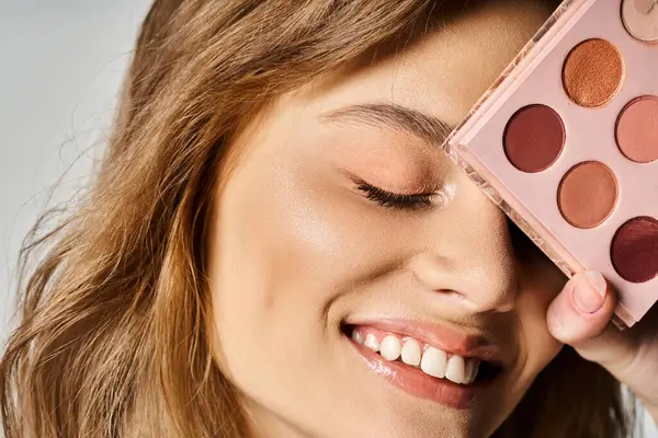 Closeup studio beauty shot of smiling woman with peach makeup palette near face with closed eyes — Stock Photo