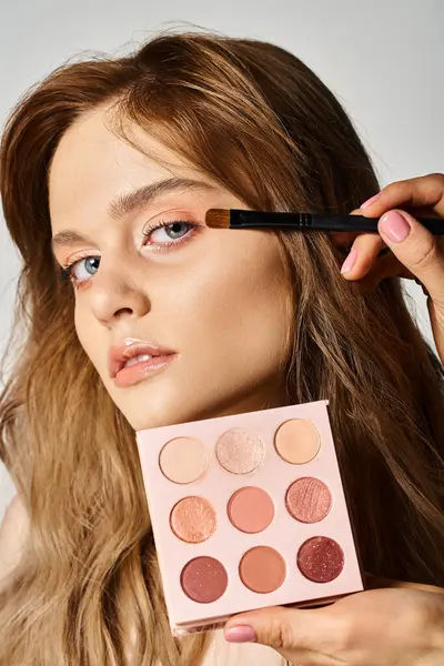 Portrait of a beautiful woman applying eyeshadow with brush on her face looking at camera — Stock Photo