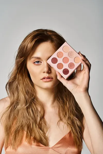 Foto de belleza de la mujer sosteniendo la paleta de maquillaje de melocotón cerca de ojo sobre fondo gris estudio — Stock Photo
