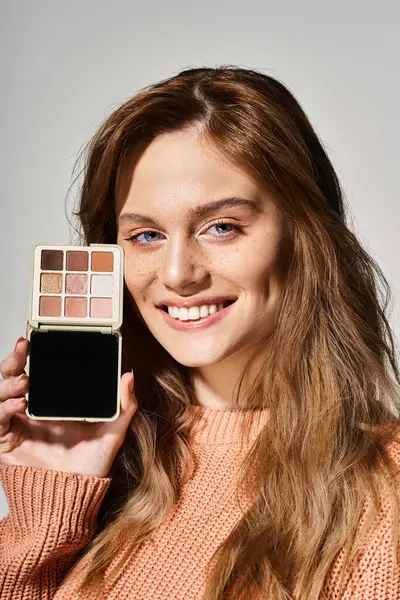 Smiling beautiful attractive woman with peach makeup palette near face on grey studio background — Stock Photo