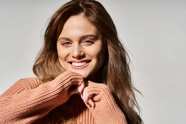 Студийный снимок улыбающейся женщины, смотрящей на камеру с натуральным макияжем, носящей свитер, трогающей подбородок — стоковое фото