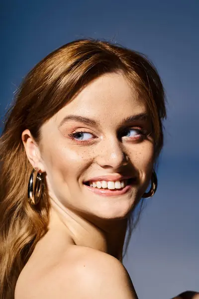 Joven mujer bastante sonriente mirando hacia otro lado con maquillaje natural melocotón desnudo, sobre fondo azul - foto de stock