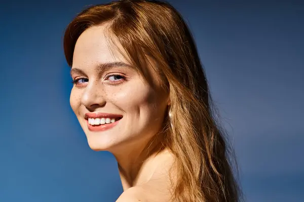 Foto vista lateral de chica sonriente con ojos azules, maquillaje desnudo melocotón con pecas sobre fondo azul - foto de stock