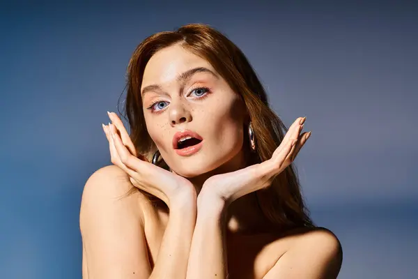 Schönheitsporträt einer überraschten jungen Frau mit blauen Augen und kinnnahen Händen auf grauem Hintergrund — Stockfoto