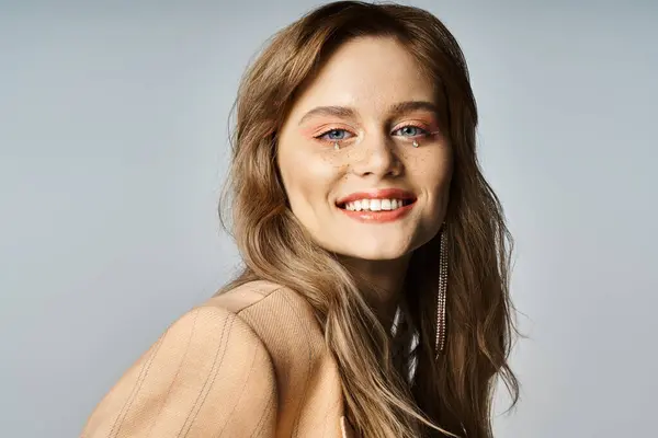 Chica sonriente en chaqueta beige, usando maquillaje desnudo con joyas de la cara, mirando a la cámara felizmente - foto de stock