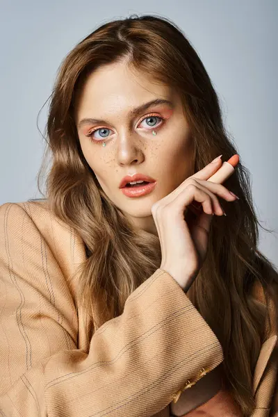 Woman with face jewels in beige jacket, holding lipstick of peach color looking at camera in studio — Stock Photo