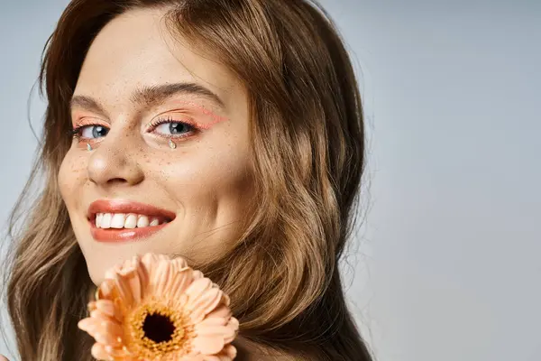 Closeup beauty shot of woman winking with peach makeup, gerbera daisy, face jewels and freckles — Stock Photo