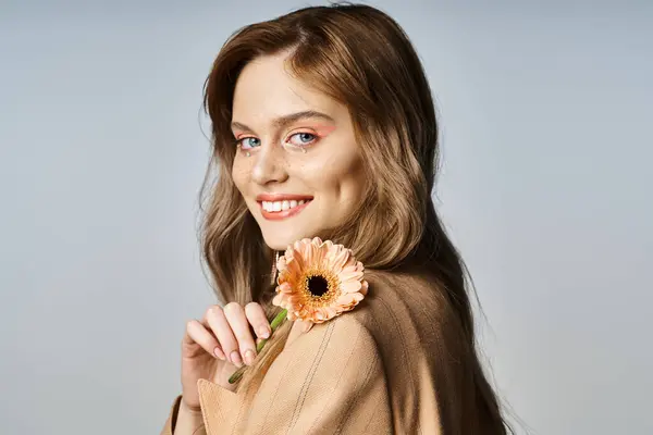 Mulher alegre atraente olhando para a câmera e segurando margarida, usando maquiagem de pêssego, jóias do rosto — Fotografia de Stock