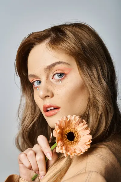 Mulher bonita olhando para a câmera e segurando margarida, vestindo maquiagem pêssego, jóias rosto — Fotografia de Stock