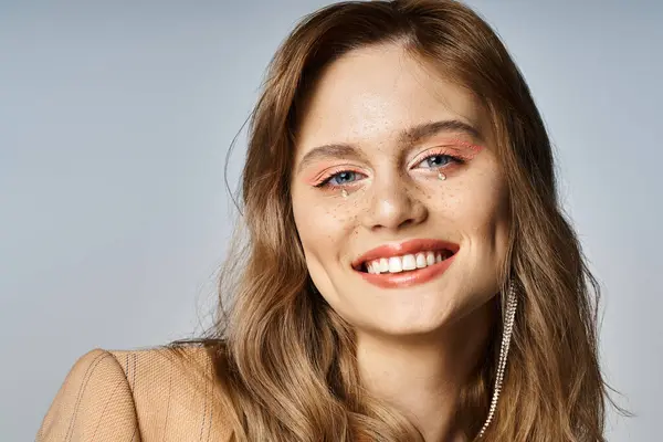 Портрет улыбающейся женщины, смотрящей в камеру, носящей персиковый макияж и украшения для лица — стоковое фото