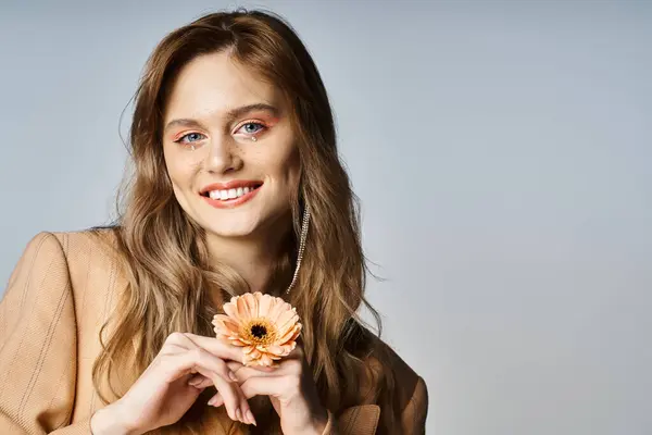 Smiling attractive woman looking at camera and holding daisy, wearing peach makeup, face jewels — Stock Photo