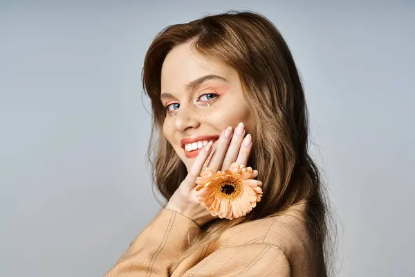 Retrato de beleza de mulher bonita com maquiagem jóias rosto e flor tocando rosto no fundo cinza — Fotografia de Stock