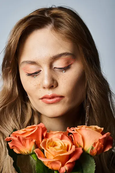 Hermosa mujer mirando rosas y usando maquillaje de melocotón desnudo y brillantes joyas de la cara - foto de stock