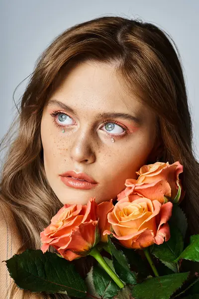 Mulher atraente com rosas perto de seu rosto e vestindo maquiagem pêssego nu e jóias rosto espumante — Fotografia de Stock