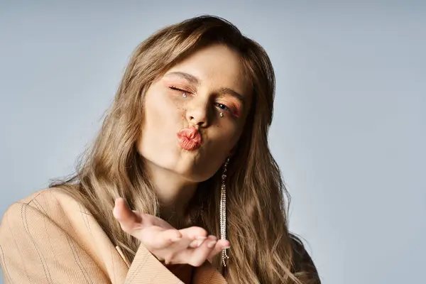 Cheerful woman wearing beige jacket, nude peach makeup and sparkling face jewels blowing kiss — Stock Photo