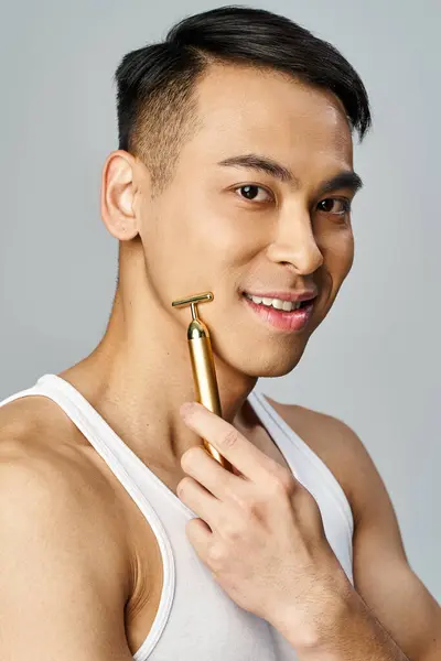 An Asian man holding a golden razor object in a grey studio, showcasing wealth and elegance. — Stock Photo
