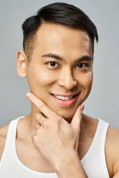A handsome Asian man with a bright smile in a grey studio, exuding joy and contentment. — Stock Photo