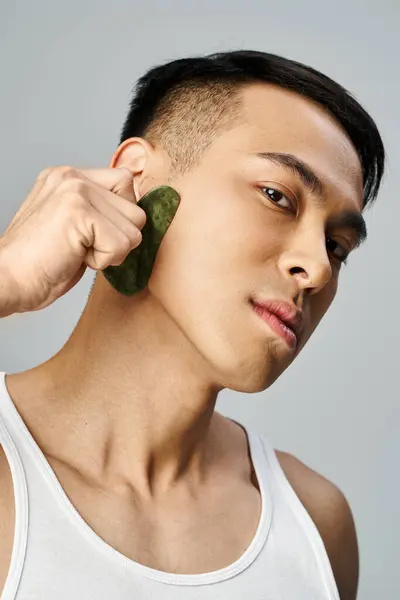 Handsome Asian man in a grey studio, holding a green gua sha on grey background — Stock Photo