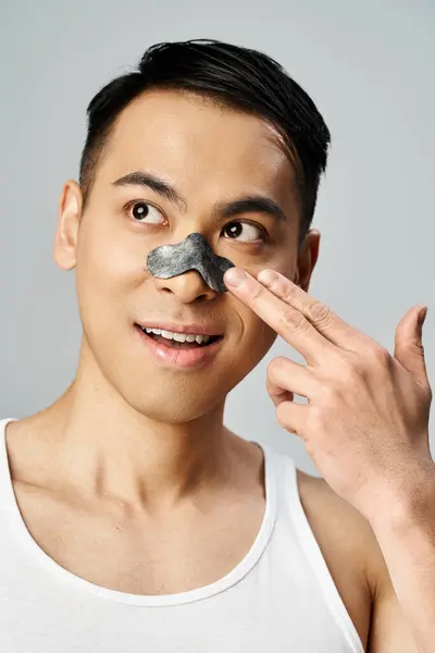Un hombre asiático guapo en un estudio gris con parche de nariz de belleza para su rutina de cuidado de la piel. - foto de stock