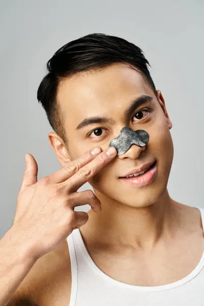 Handsome Asian man in grey studio wearing a nose patch during beauty routine. — Stock Photo