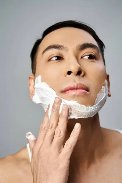 Bonito homem asiático com espuma de barbear no rosto em um estúdio cinza. — Stock Photo