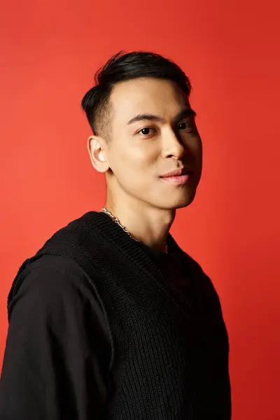 Handsome Asian man exudes charm in a black, standing confidently against a striking red backdrop in a studio setting. — Stock Photo