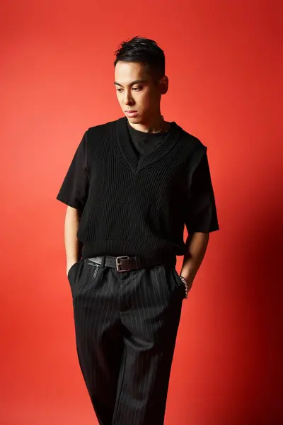 Стильный и красивый азиат в черной рубашке и брюках уверенно стоит на ярком красном фоне. — стоковое фото