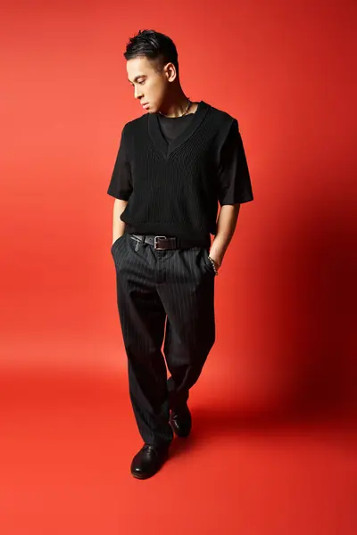 Un Asiatique élégant et beau en tenue noire pose en toute confiance devant un fond rouge saisissant dans un décor de studio. — Photo de stock