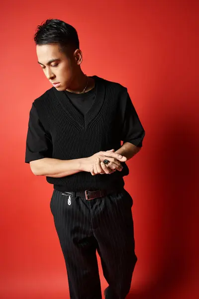 A stylish and handsome Asian man in a black sweater and pants poses against a vibrant red background in a studio setting. — Stockfoto