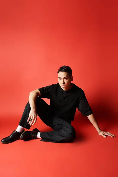 Красивый азиатский мужчина в стильной черной одежде сидит на земле со скрещенными ногами, источая спокойствие и спокойствие. — стоковое фото
