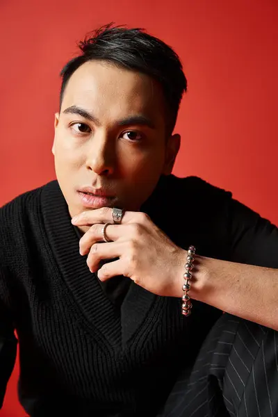 Un homme asiatique élégant et beau en tenue noire mettant fièrement en valeur une bague à son doigt sur un fond rouge vif. — Photo de stock