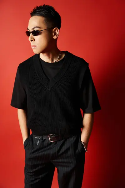 A stylish and handsome Asian man dressed in all black poses against a striking red background in a studio setting. — Stock Photo