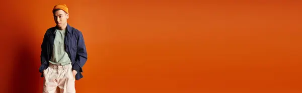 A handsome Asian man stands confidently in front of a vibrant orange wall, exuding style and charisma. — Stock Photo
