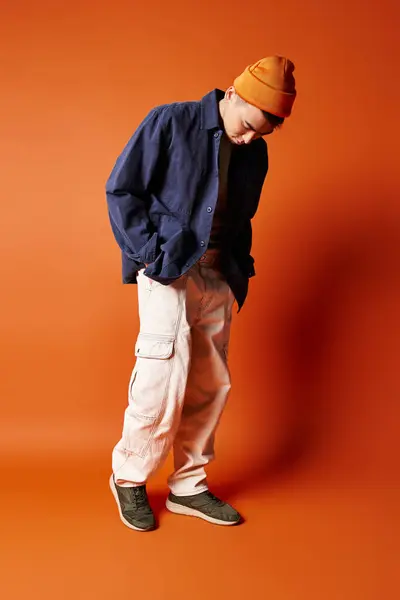 Hombre asiático guapo con una camisa azul elegante y pantalones blancos, golpeando una pose segura contra un fondo naranja en un estudio. - foto de stock